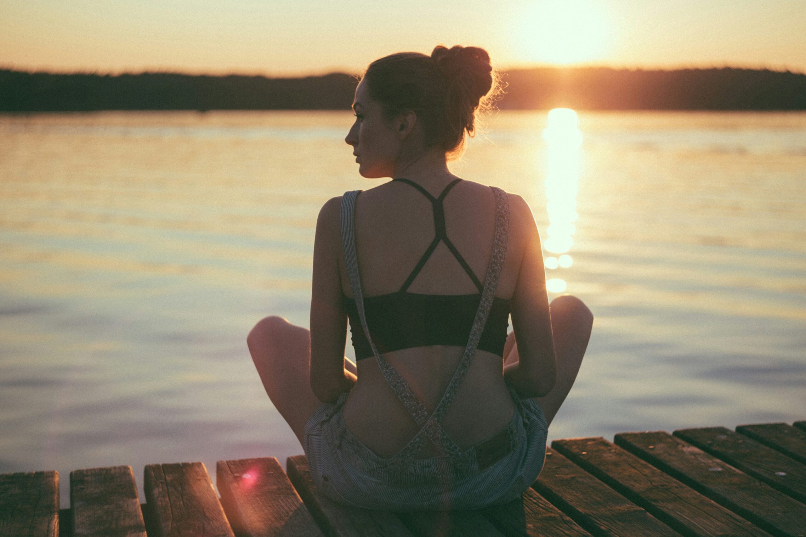 woman sitting on brown wooden dock during sunset